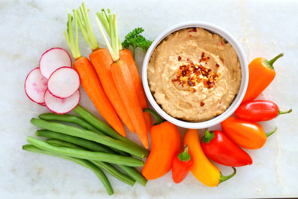 Hummus with fresh vegetables, above view on white marble