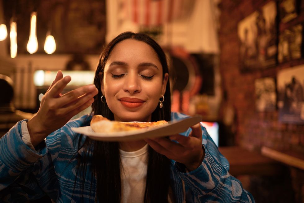 hungry woman with delicious pizza, food or consumables at a bar, restaurant or diner at night one happy and casual girl, foodie or tourist enjoying a dinner meal at a local trendy location