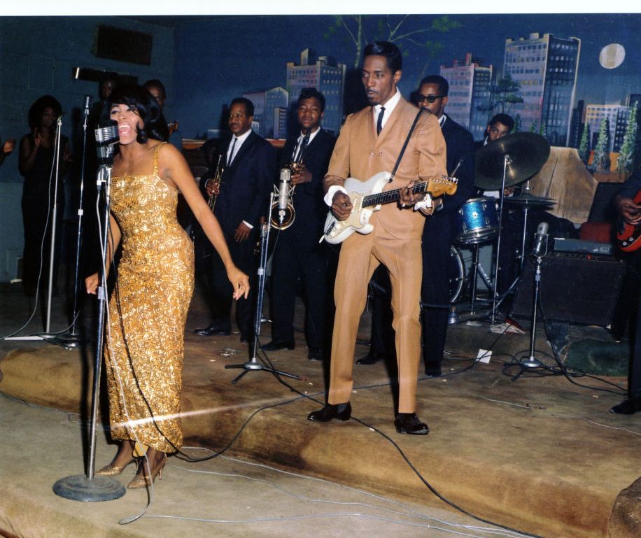 tina turner sings at a microphone as ike turner plays electric guitar