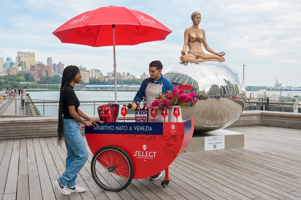 a woman standing next to a man sitting on a bicycle with a red umbrella