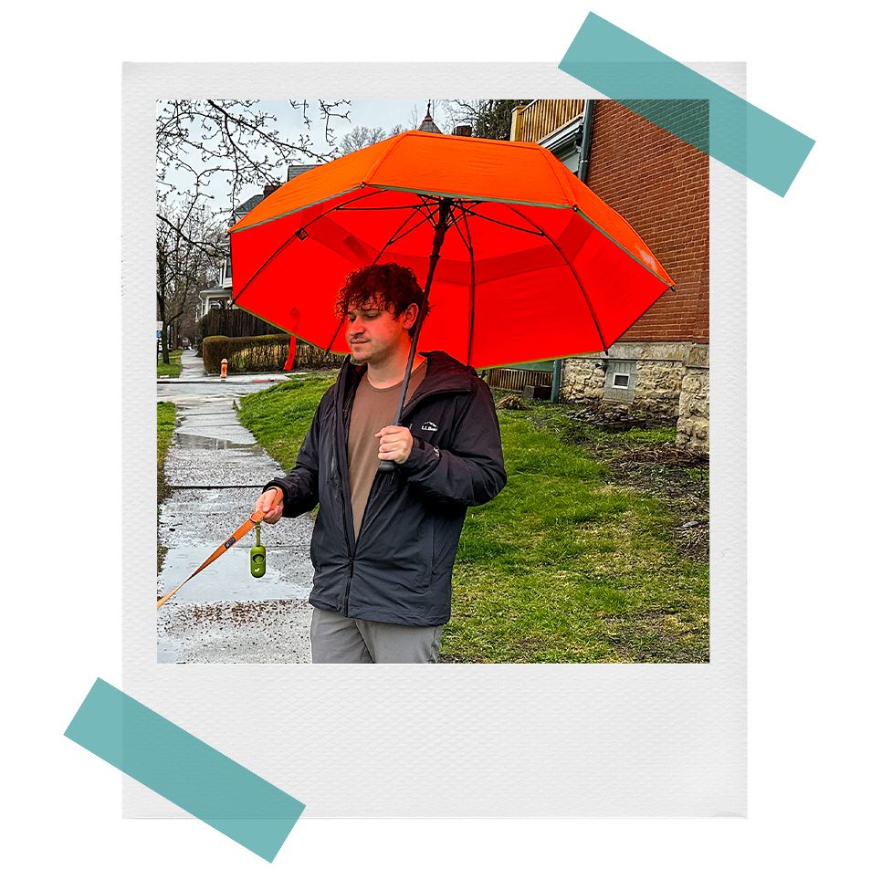 weatherman travel umbrellas open on the sidewalk together, and brnadon using an orange weatherman travel umberlla outside in the rain