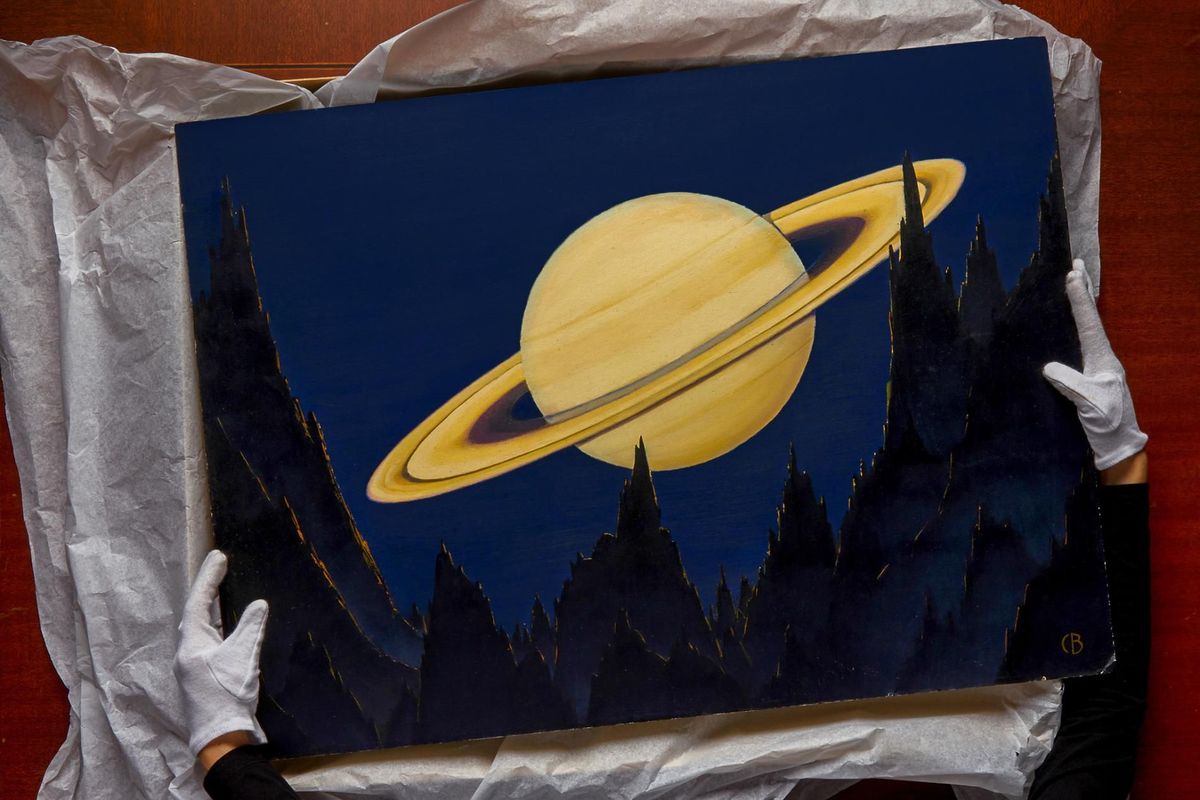 Senior fotoarchivaris Sara Manco houdt een schilderij van Charles Bittinger omhoog waarop Saturnus vanaf een asterode is te zien Het schilderij verscheen in 1939 als illustratie bij een artikel in National Geographic