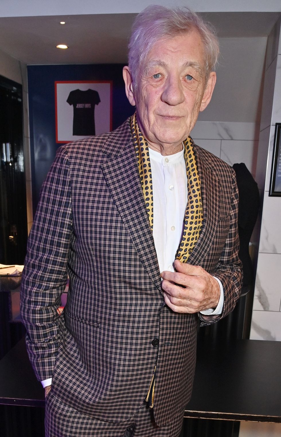 sir ian mckellen in a checkered pattern suit as he goes to collect the special recognition award at the pantomime awards 2023