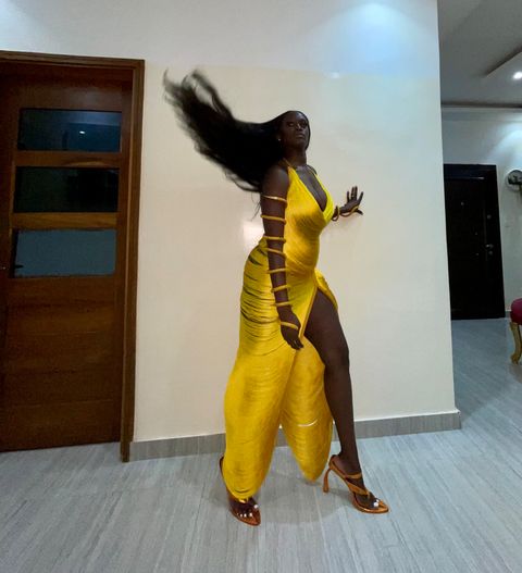 a black woman with long hair wears a yellow gown with a slit