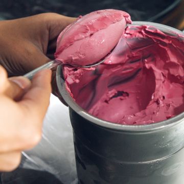 scooping homemade raspberry ice cream out of stainless steel bowl