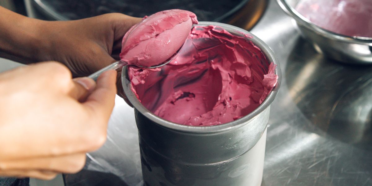 scooping homemade raspberry ice cream out of stainless steel bowl