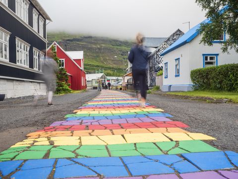 iceland, seydisfjordur, people walking along rainbow colored asphalt road in middle of remote town