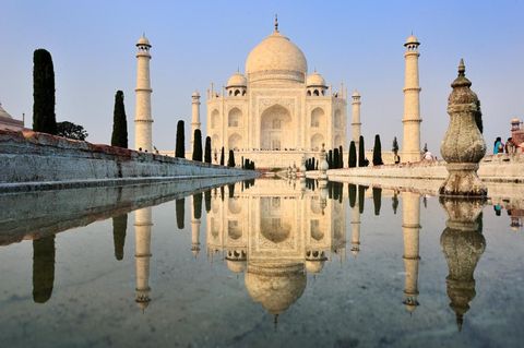 De Taj Mahal is beroemd vanwege zijn schoonheid beroemd als symbool van de eeuwige liefde maar vooral beroemd om zijn beroemdheid Zelfs als het geen perfecte symmetrie in steen zou zijn de verhoudingen elegant bijgewerkt in eeuwen van monumentale bouwkunst onder de Mughal vorsten van centraal India zou de Taj Mahai ons nog steeds verleiden als plaats in de geschiedenis van de wereldreizen Eeuwenlang was het de must see toeristenattractie ter wereld Miljoenen fotos zijn genomen vanaf exact hetzelfde punt aan de spiegelende vijver Op een bepaalde manier is het nemen van de foto op zich een pelgrimstocht zelf in het echt zien wat miljoenen anderen ook hebben gezienIconisch beeld Over de spiegelende vijver met de Taj tussen de minaretten
