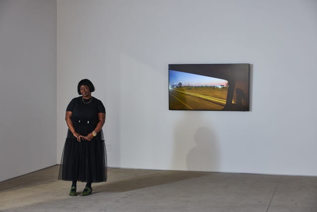a woman standing in front of a photograph of a road and sunset