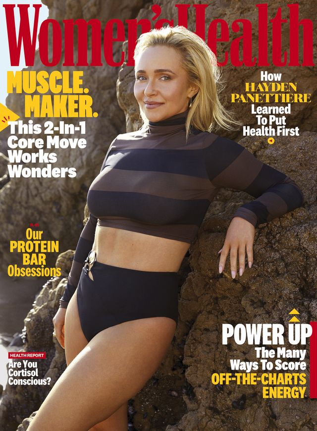 women's health cover with celebrity hayden panettiere, wearing a brown and black striped cropped turtleneck and black bikini bottoms, smiling next to rocks on the beach