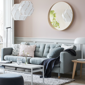 living room with pink walls, bluegray couches, floor lamps, side table with white lamp, mounted circular mirror