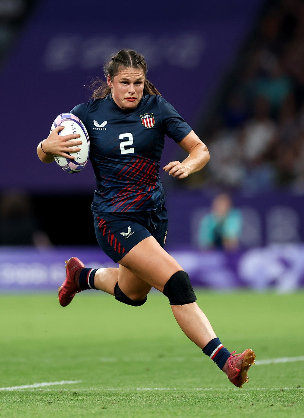 ilona maher running while cradling a rugby ball in her right arm and wearing her no 2 usa jersey