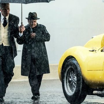 a man in a suit and tie walking next to a yellow car