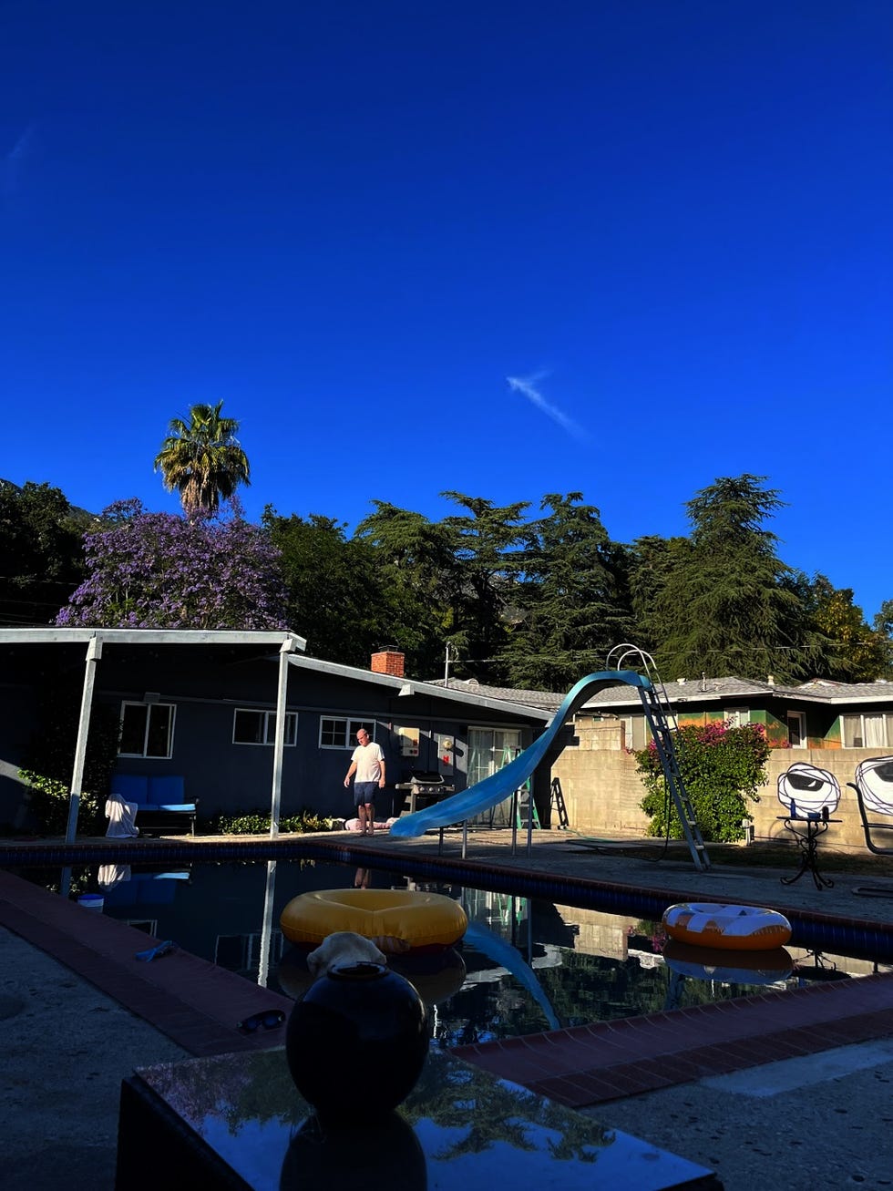 escena de una piscina al aire libre con un hombre parado cerca y un tobogán