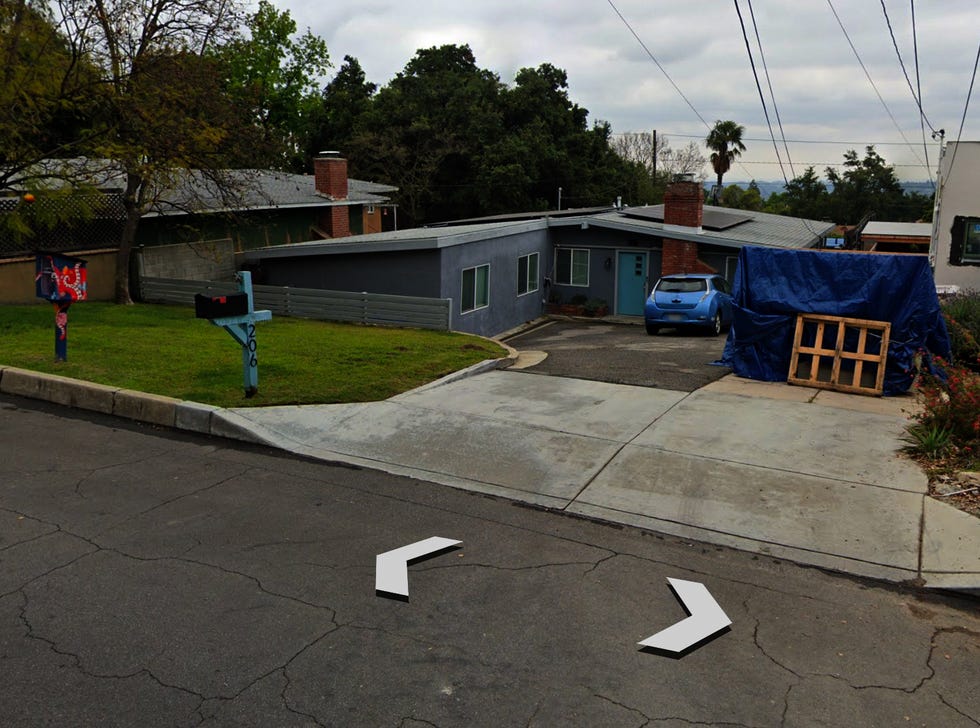 casa residencial con un automóvil azul en la entrada y una estructura cubierta con una lona