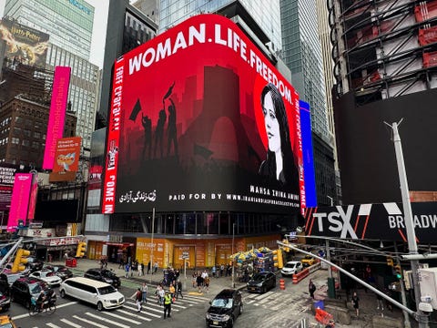 billboard in times square showing mahsa amini, the words woman life freedom, and black illustrated silhouettes of protestors,