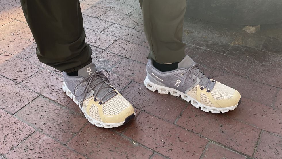 a tester wearing grey and yellow on cloud 5 sneakers on a brick sidewalk as part of good housekeeping's testing for the best walking shoes for men