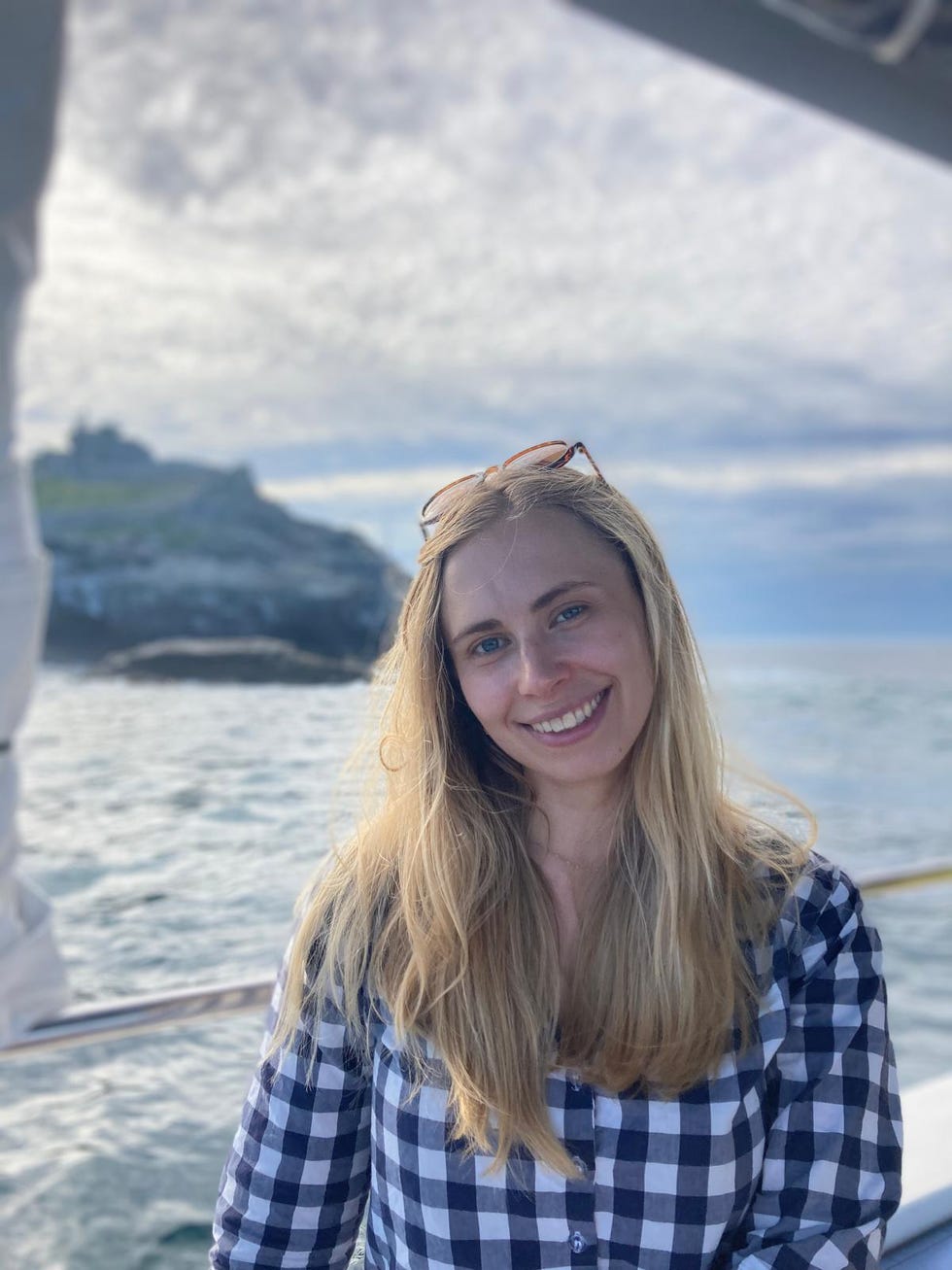 person with long hair wearing a checkered shirt on a boat by the sea