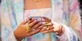 fashionable woman with purple nail polish and a lot of gold rings typing on her phone, wearing a three piece rainbow clothing set