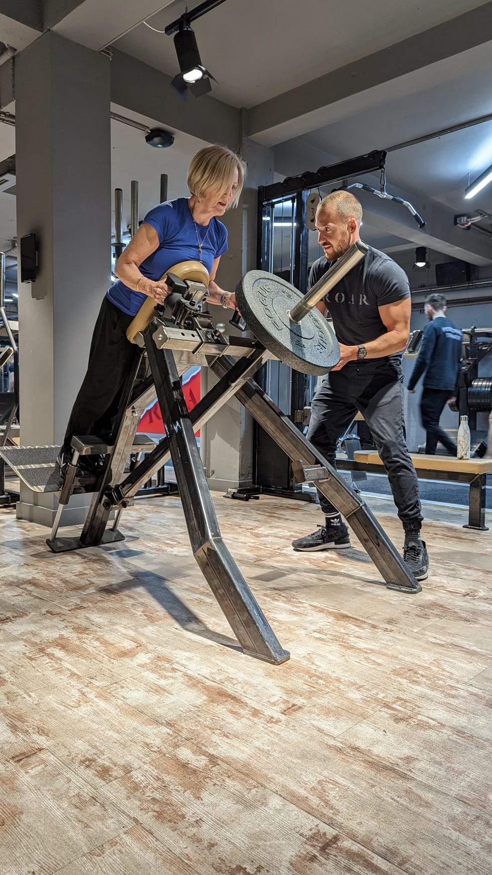 woman using weights machine in gym with personal trainer