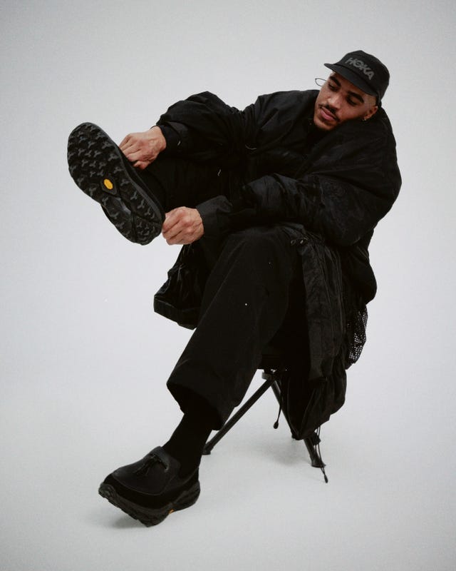 person seated in a chair wearing all black clothing and adjusting shoes
