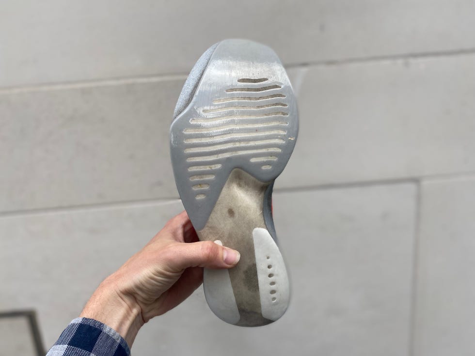 sole of a sneaker held by a hand against a neutral background
