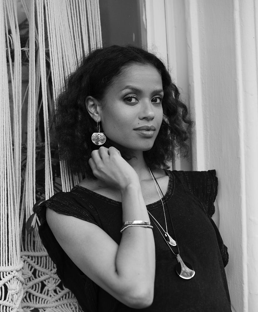 person with curly hair wearing jewelry posing against a backdrop of strings
