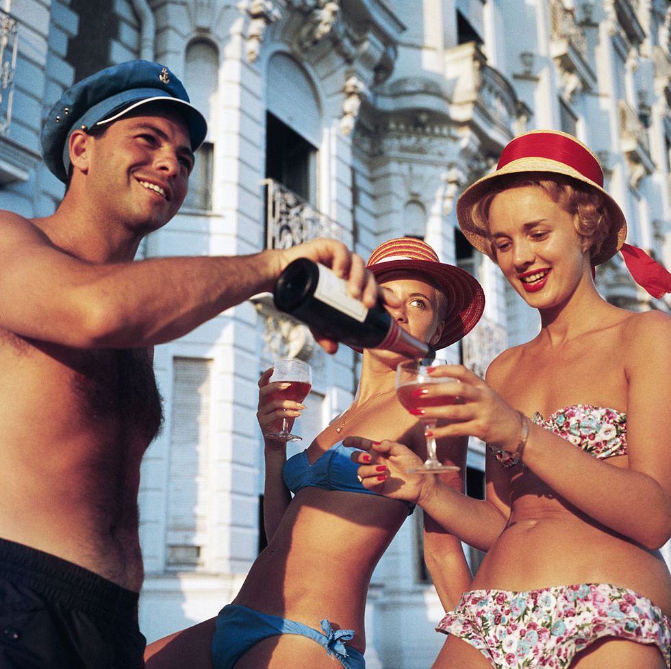 1958  swimsuited revellers enjoy a glass of wine outside the carlton hotel, cannes  photo by slim aaronsgetty images