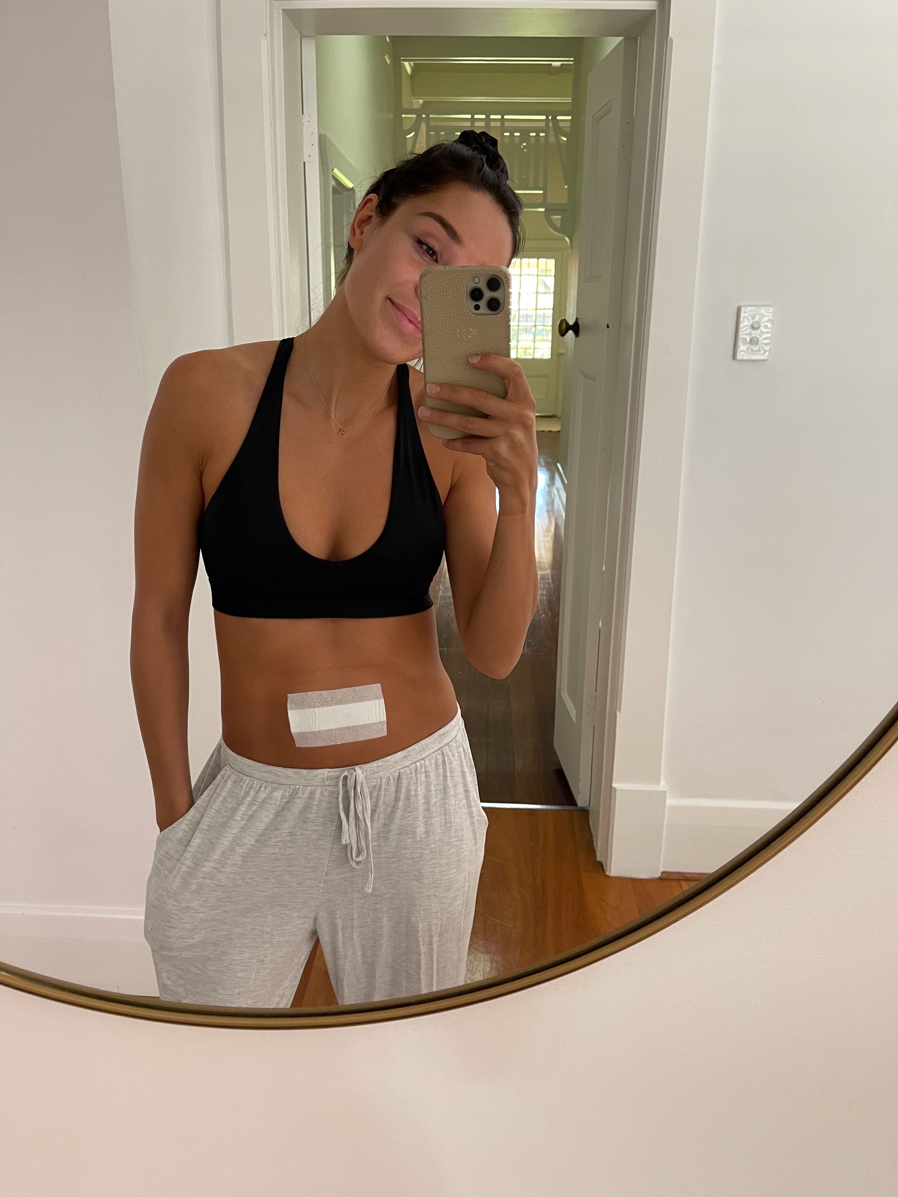 kayla itsines posing in a mirror with a bandage on her stomach
