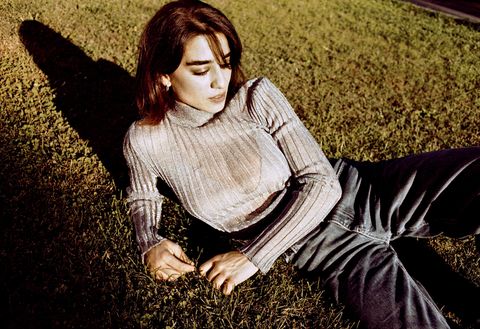simona poses laying in grass, wearing a gray long sleeve top with jeans
