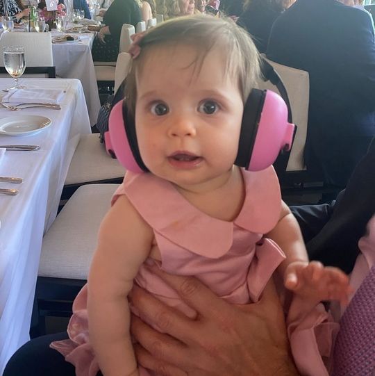 a baby wears pink noise cancelling headphones at a noisy family event