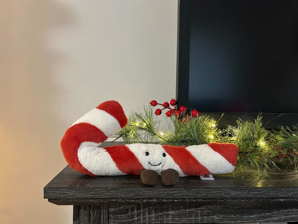 a plush candy cane with a smiling face placed on a table with festive decorations