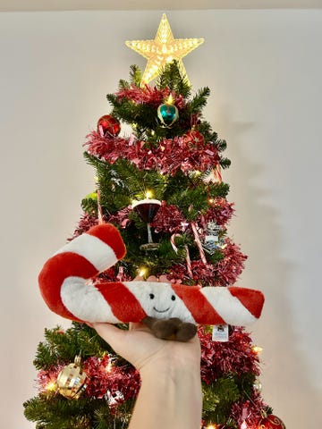 a hand holding a plush candy cane in front of a decorated christmas tree