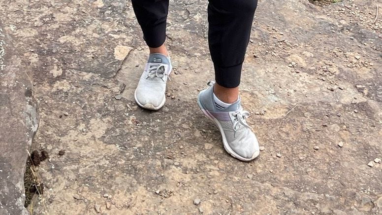 a person's legs and feet modeling new balance sneakers against a rocky background