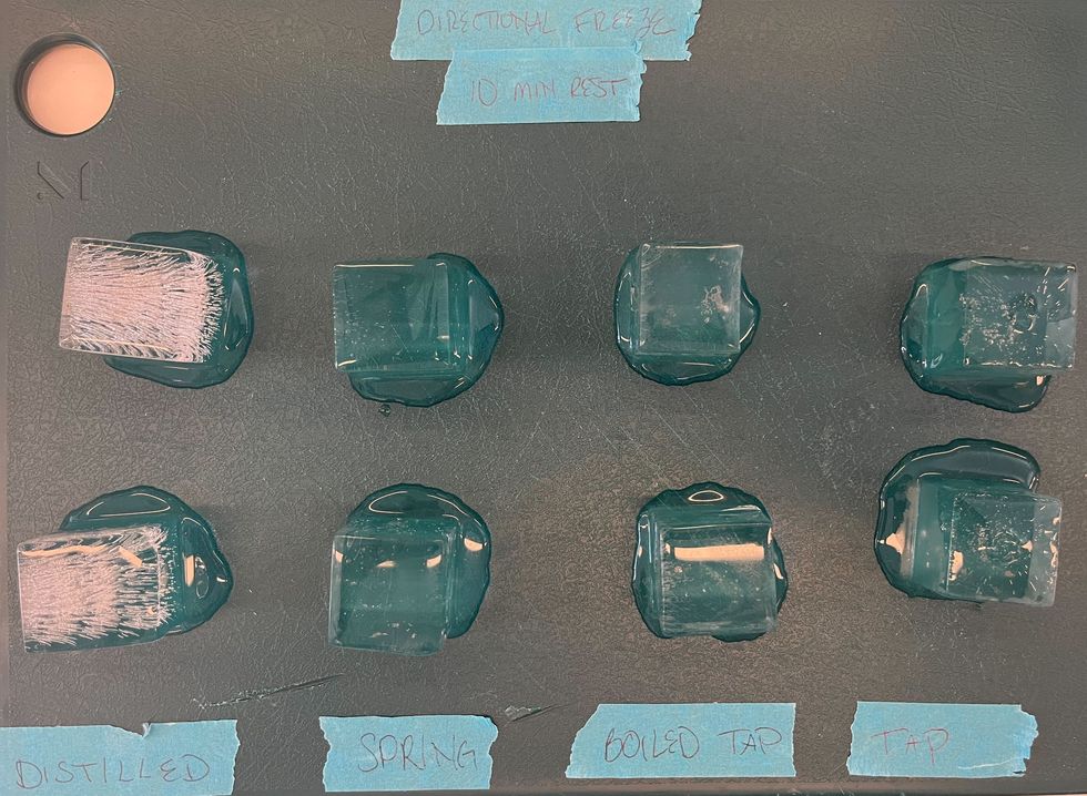 four columns of square ice cubes on a green cutting board with blue tape labels