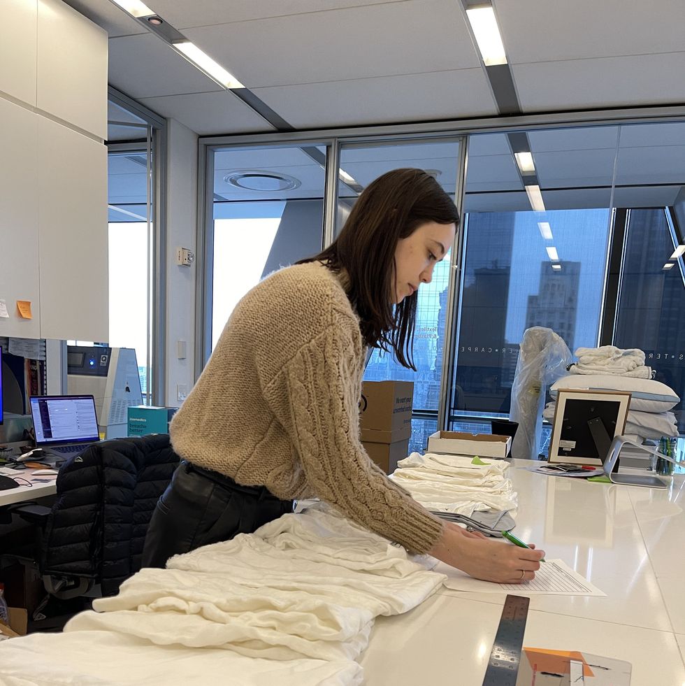 a woman touching one fabric sample from a row of different white sheet fabrics to evaluate softness and feel