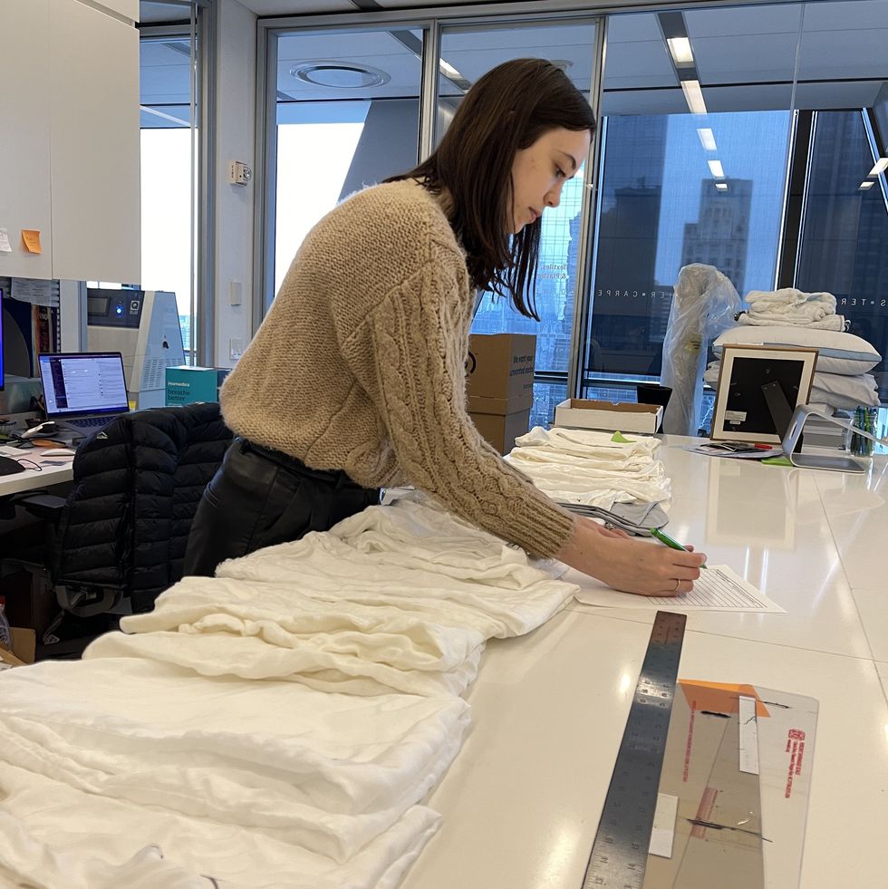a woman touches one fabric sample from a row of different white sheet fabrics to evaluate softness and feel