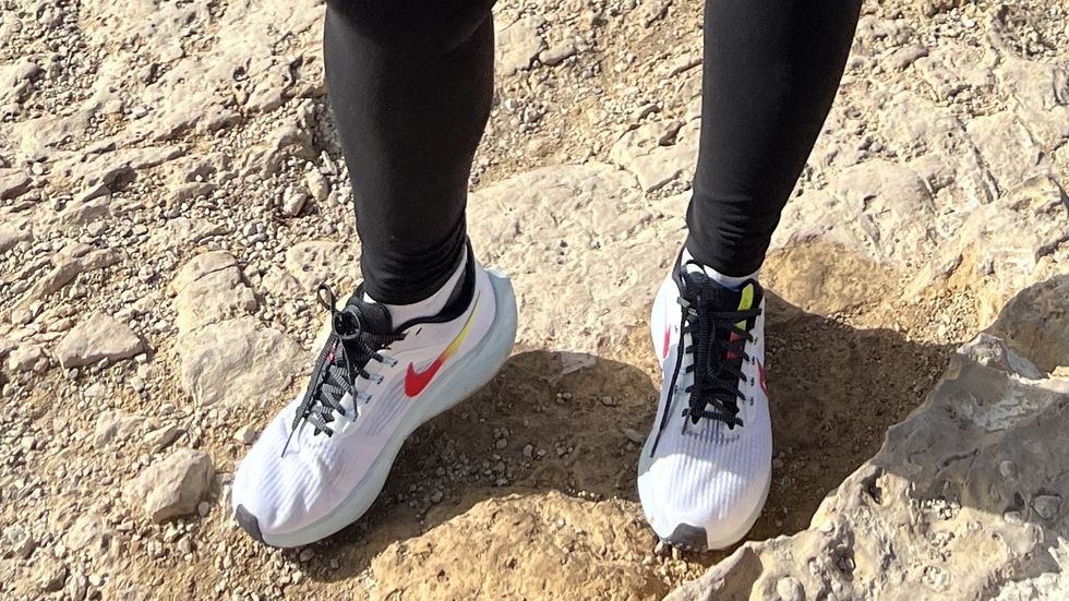 a person posing on a rock with nike pegasus sneakers, good housekeeping's testing for best walking shoes for women