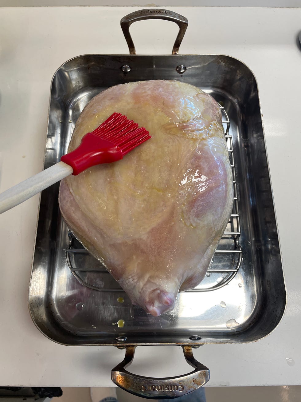 brushing oil on a frozen turkey in a roasting pan