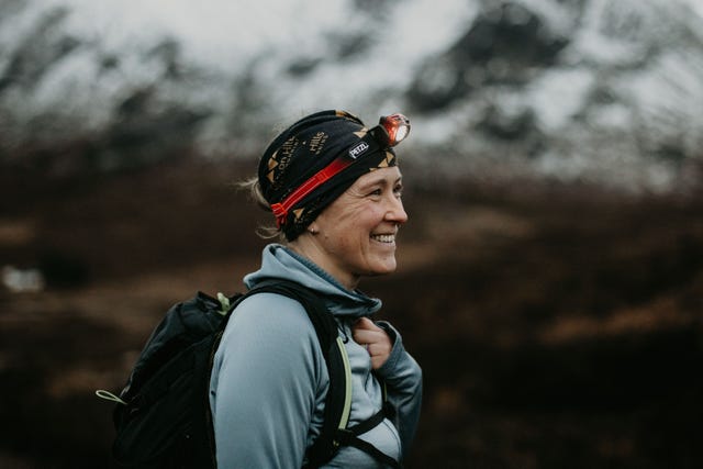 smiling trail runner wearing a bag and head torch in a mountain environment