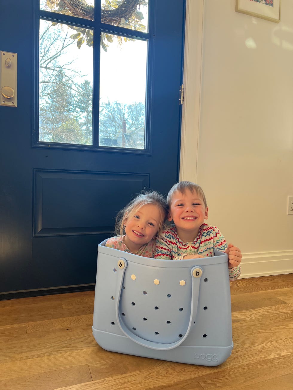 two children sitting in a large blue tote bag