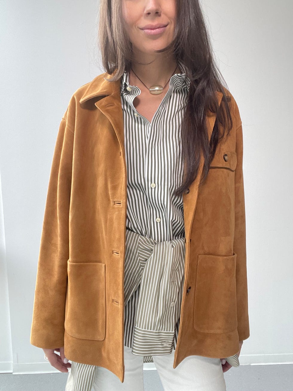 a person wearing a brown suede jacket over a striped shirt and white pants
