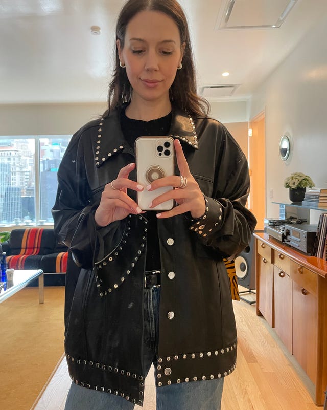 person holding a smartphone in front of a mirror wearing a studded black shirt jacket and jeans person holding a smartphone in front of a mirror wearing a studded black shirt jacket and jeans