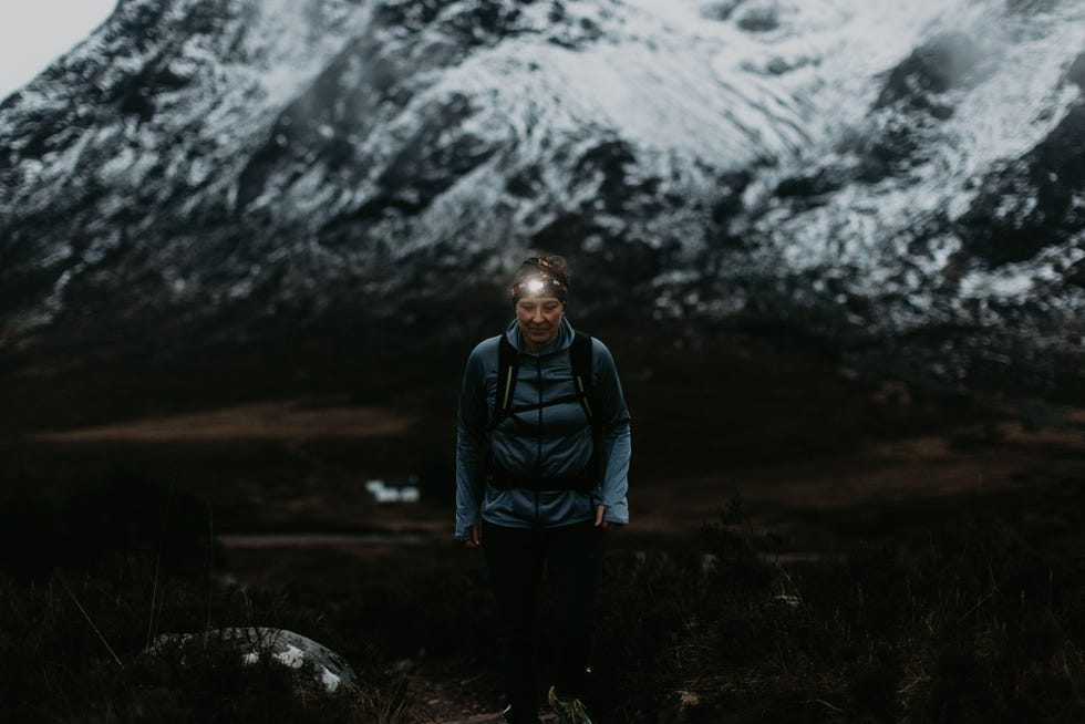 a person stands on a trail in a mountainous landscape with snowcapped peaks in the background