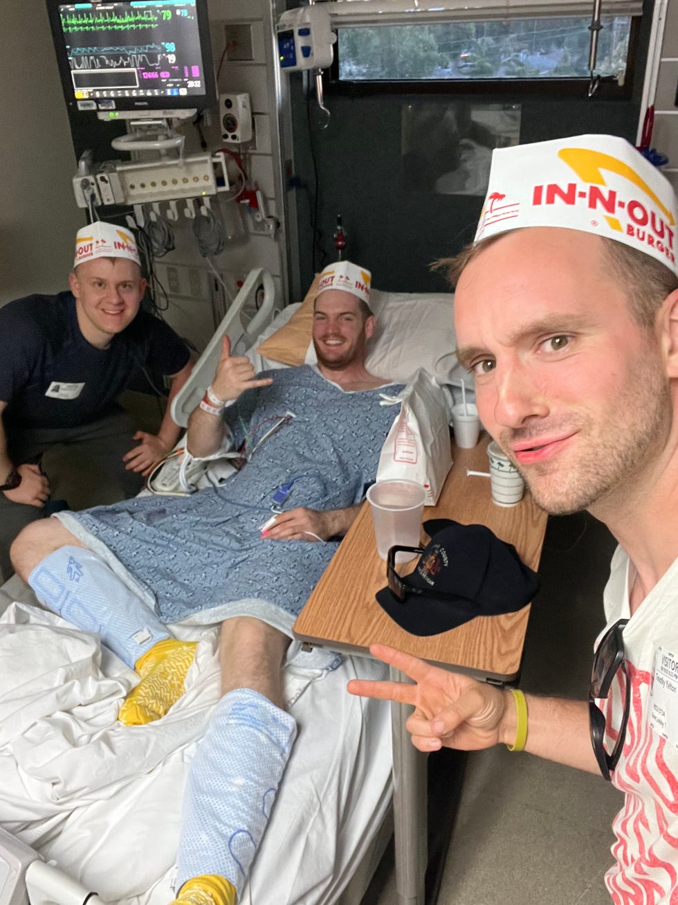 Stewart in a hospital bed with friends and In-N-Out hats