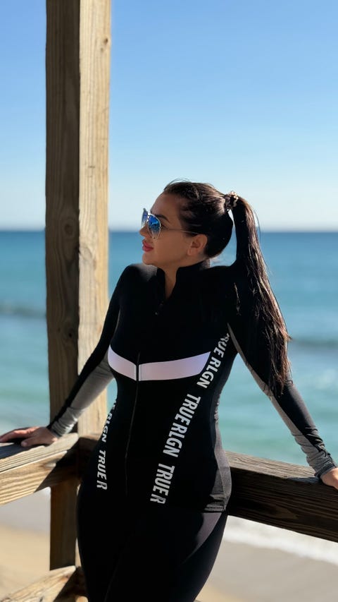 person in a black swimming suit leaning against a wooden structure by the ocean
