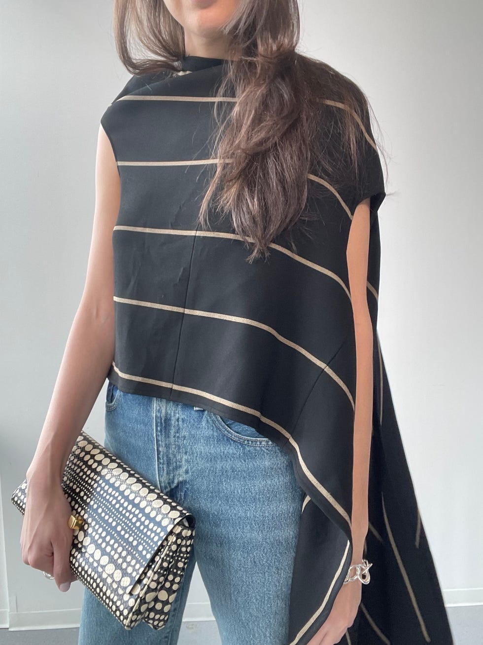 woman wearing a black top with golden stripes and blue jeans holding a patterned clutch