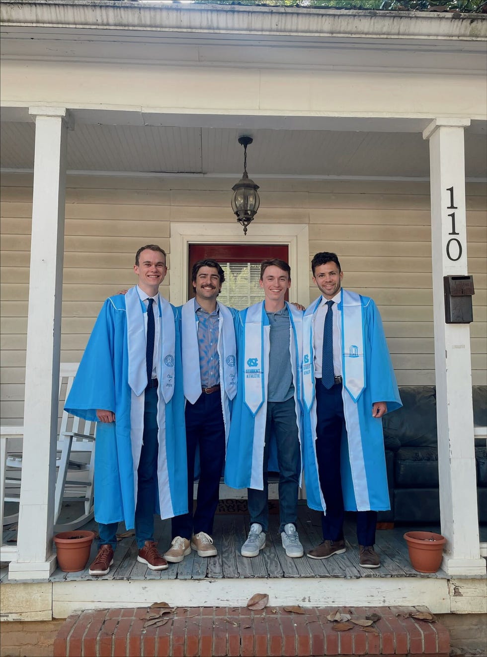 group of graduates in caps and gowns standing on a porch