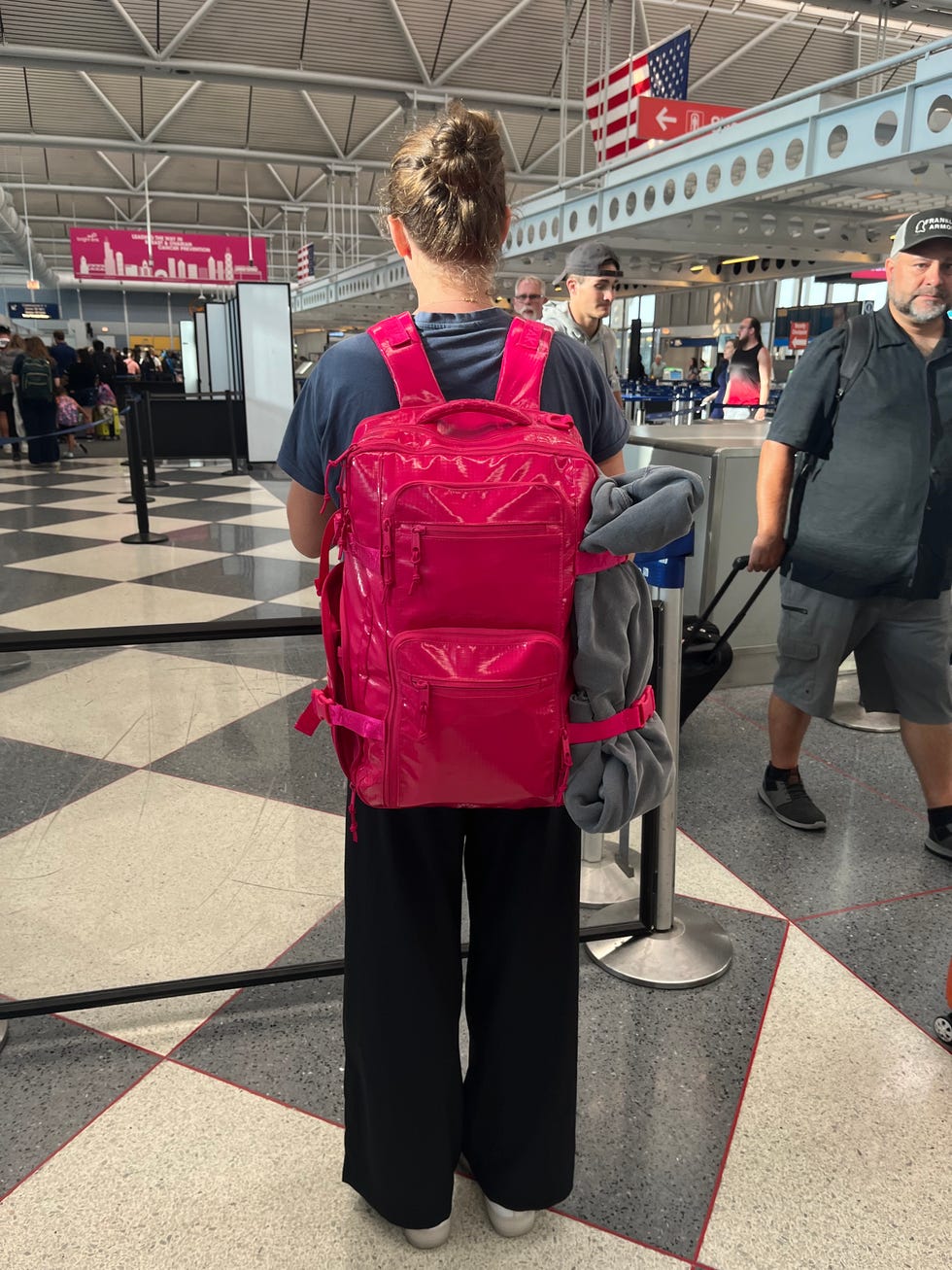 a tester wearing a pink calpak 26l terra backpack in an airport, good housekeeping's best carry on backpacks