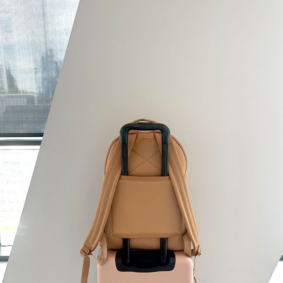 a tan backpack with a luggage sleeve on a pink carry on suitcase
